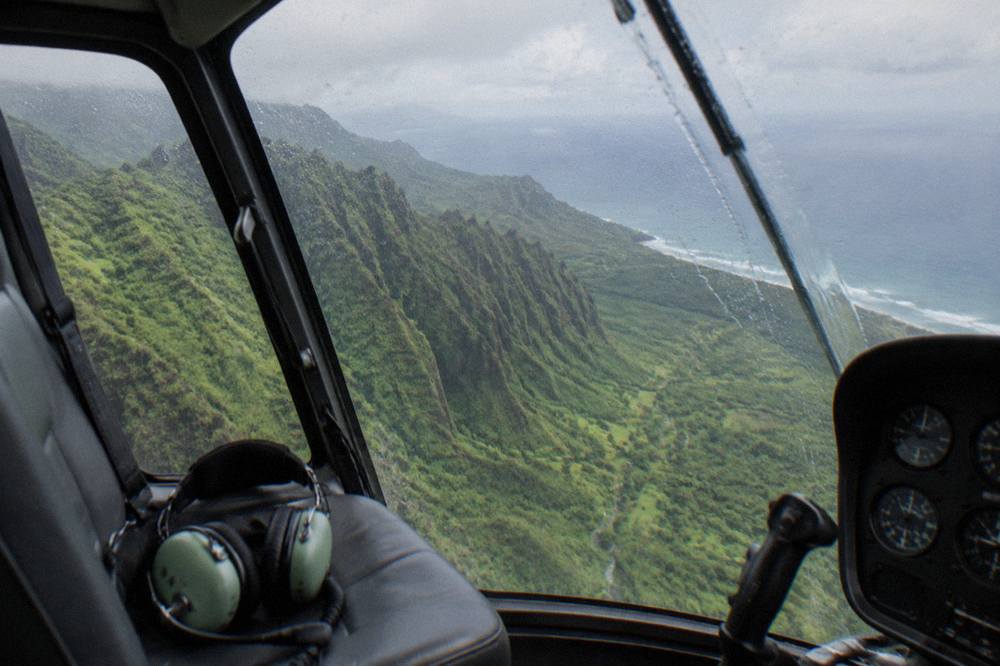 A helicopter cockpit view of a deep green valley and ocean horizon