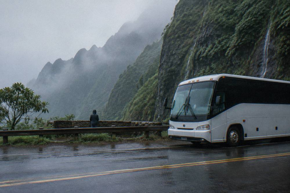 A large tour bus on a road beside green Kauai cliffs