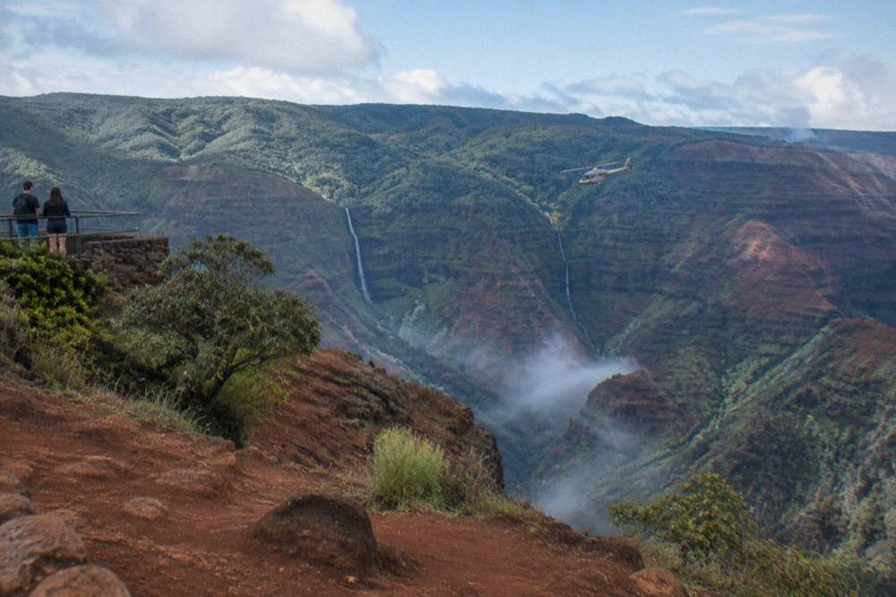 A helicopter flying over deep green valleys with thin waterfalls on canyon walls