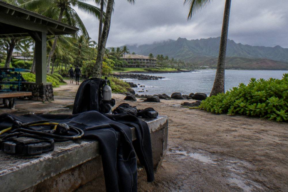 Scuba gear laid out on a bench beside a shaded dive staging area