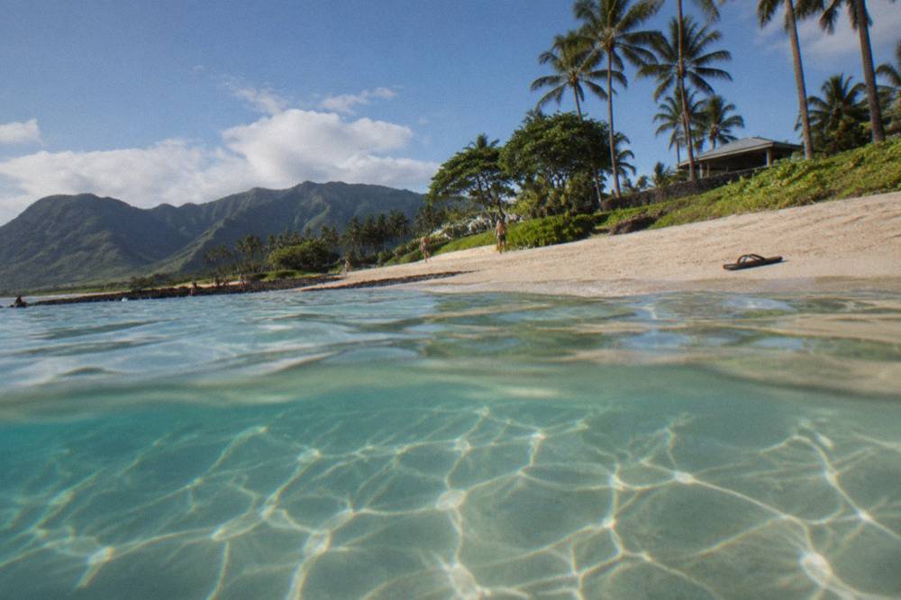 Calm waist-deep turquoise water over sand near a beginner surf break