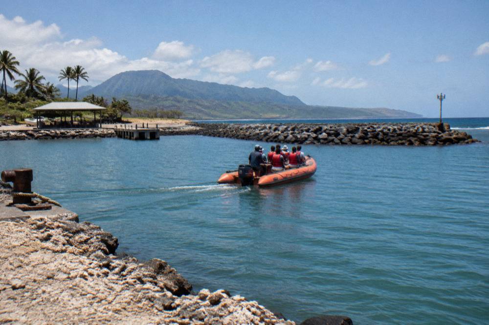 A rugged zodiac raft holding people in life vests cruising close to tall sea cliffs
