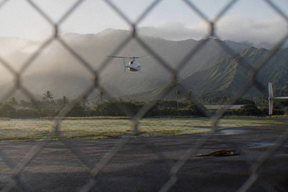 A helicopter flying over a tall narrow waterfall pouring down a green cliff face