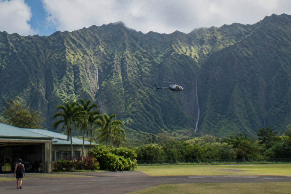 A helicopter flying past tall white waterfalls streaming down a dark green cliff wall