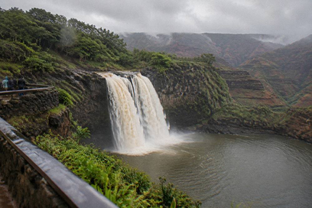 A full wide waterfall pouring over a dark rock ledge into a large calm pool