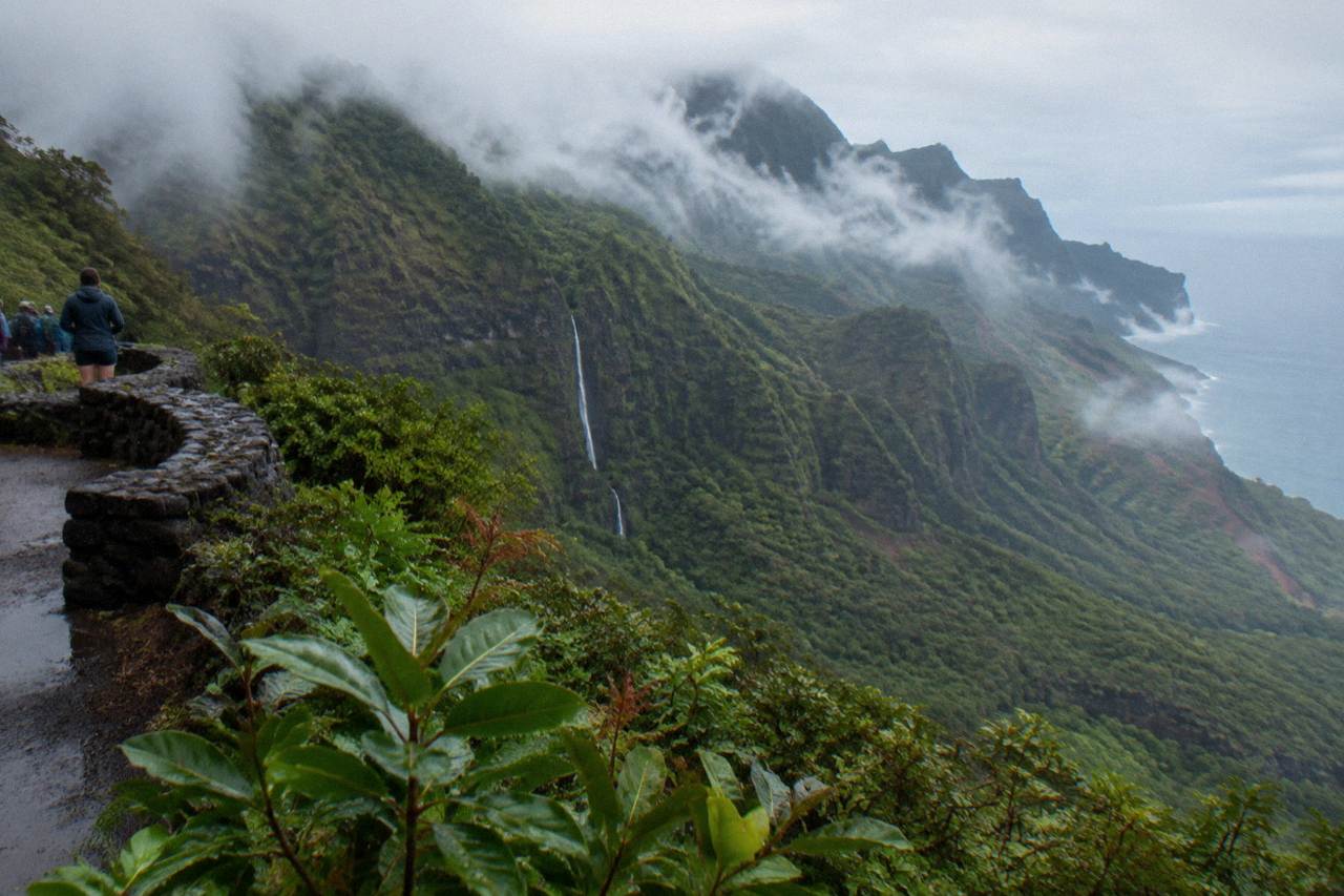 A tall ribbon waterfall dropping down a green cliff face covered in dense tropical vegetation