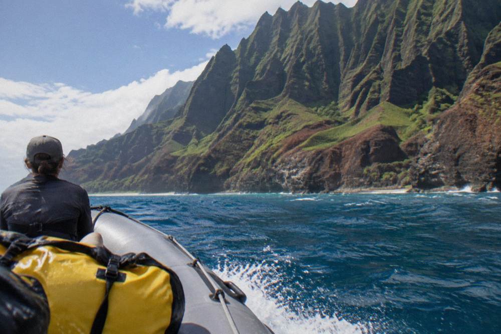 A small raft cruising close to sheer sea cliffs on the Na Pali coast