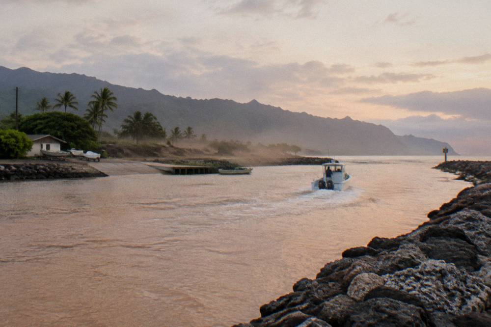 A tour boat leaving a small harbor past a breakwater in early morning light
