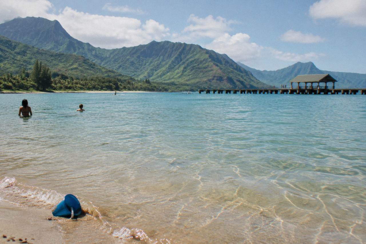 A calm Kauai beach cove with turquoise shallows and green cliffs in the background