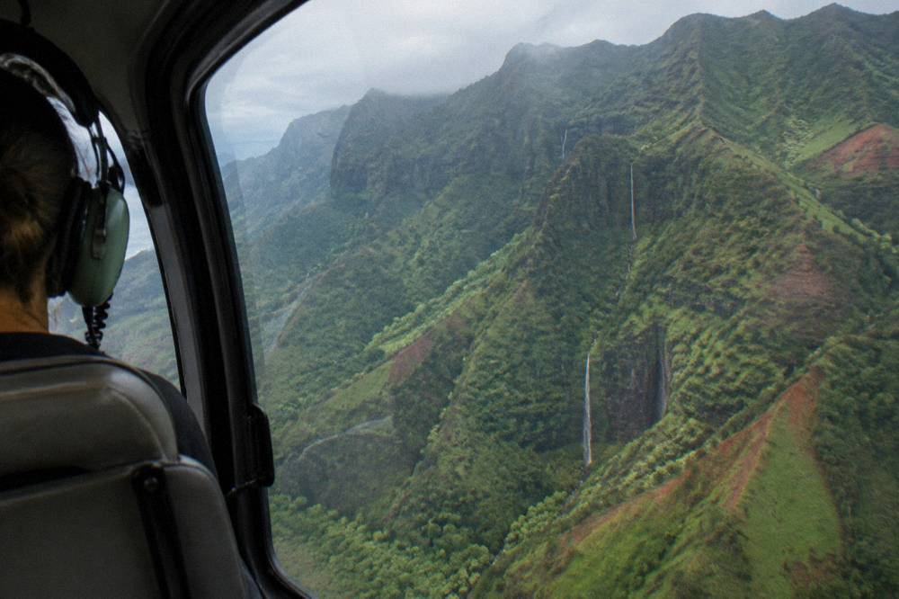 A helicopter flying over deep green folded valleys and thin waterfalls on Kauai