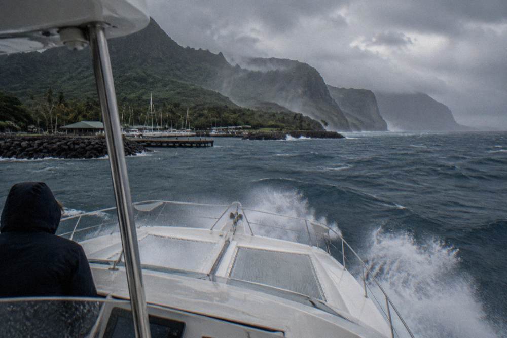 A catamaran cutting through open ocean swells with whitecaps near distant cliffs