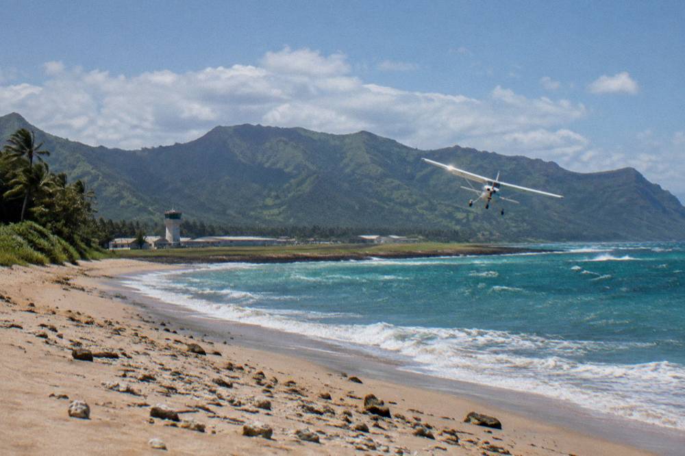 A small airplane banking over a long empty beach and turquoise water on Kauai