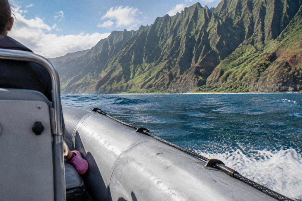 A small raft cruising along the base of green sea cliffs on the Na Pali Coast