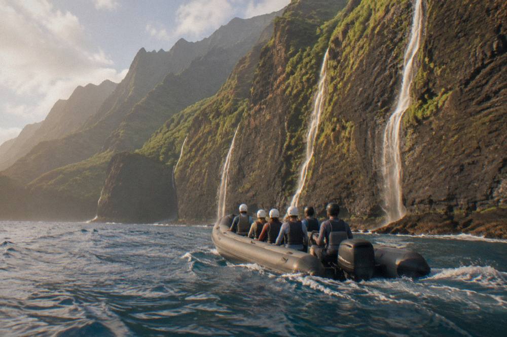 A rigid inflatable raft cruising close to the vertical sea cliffs of the Na Pali coast