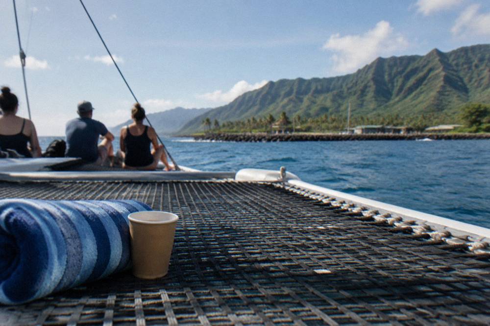 Passengers seated on the shaded trampoline deck of a catamaran in calm blue water