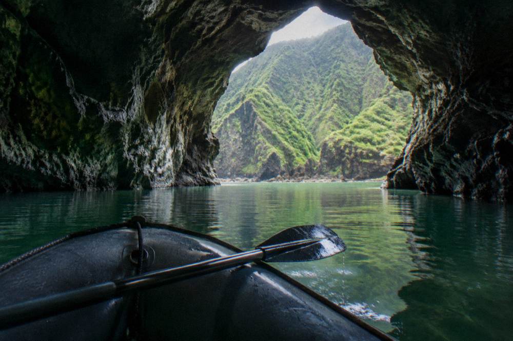 A zodiac raft floating inside a dark sea cave opening along a rocky coastline