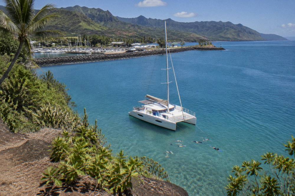 A catamaran at anchor in a clear bay with snorkelers in the water near the bow