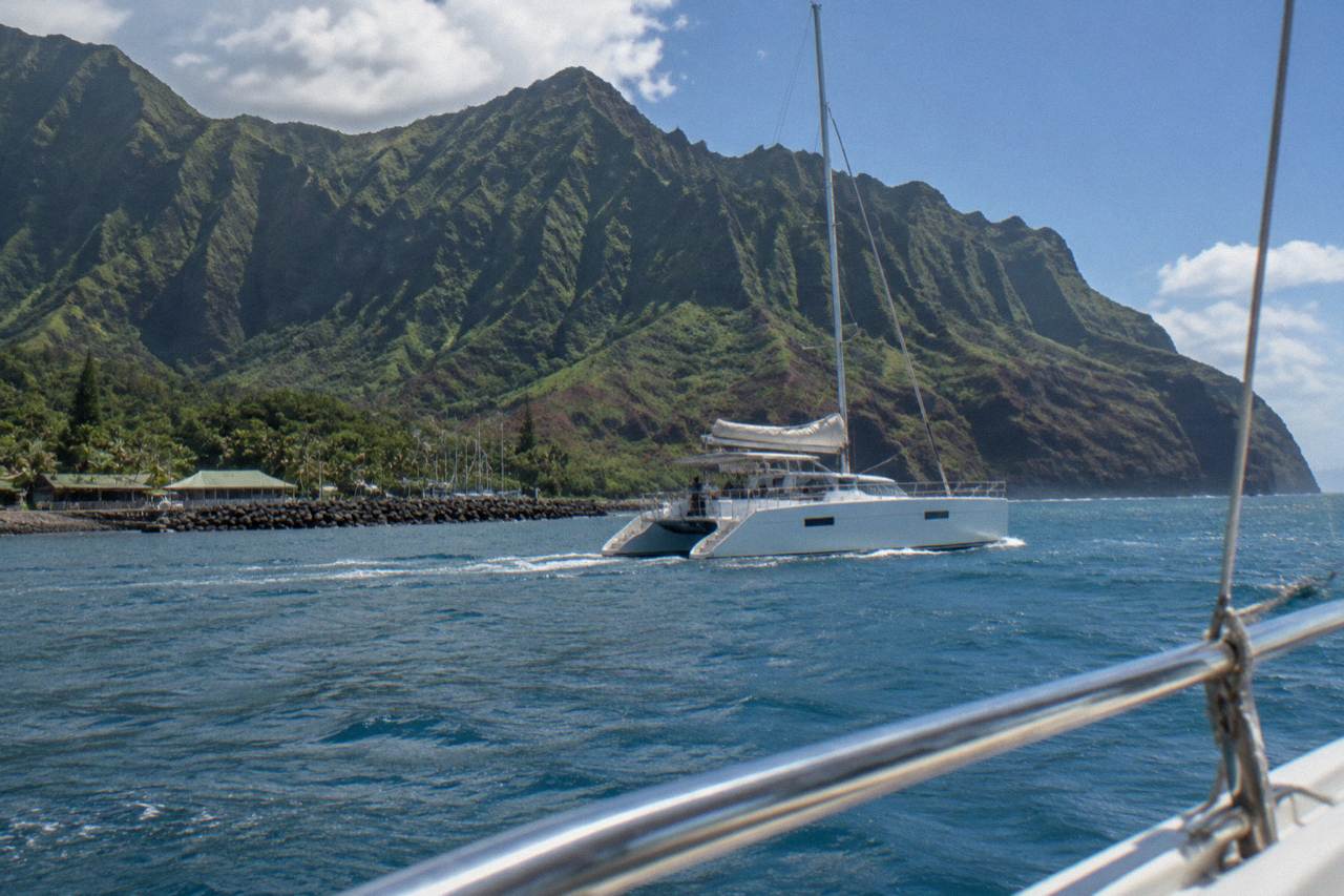 A catamaran cruising along the green sea cliffs of the Na Pali coast at midday