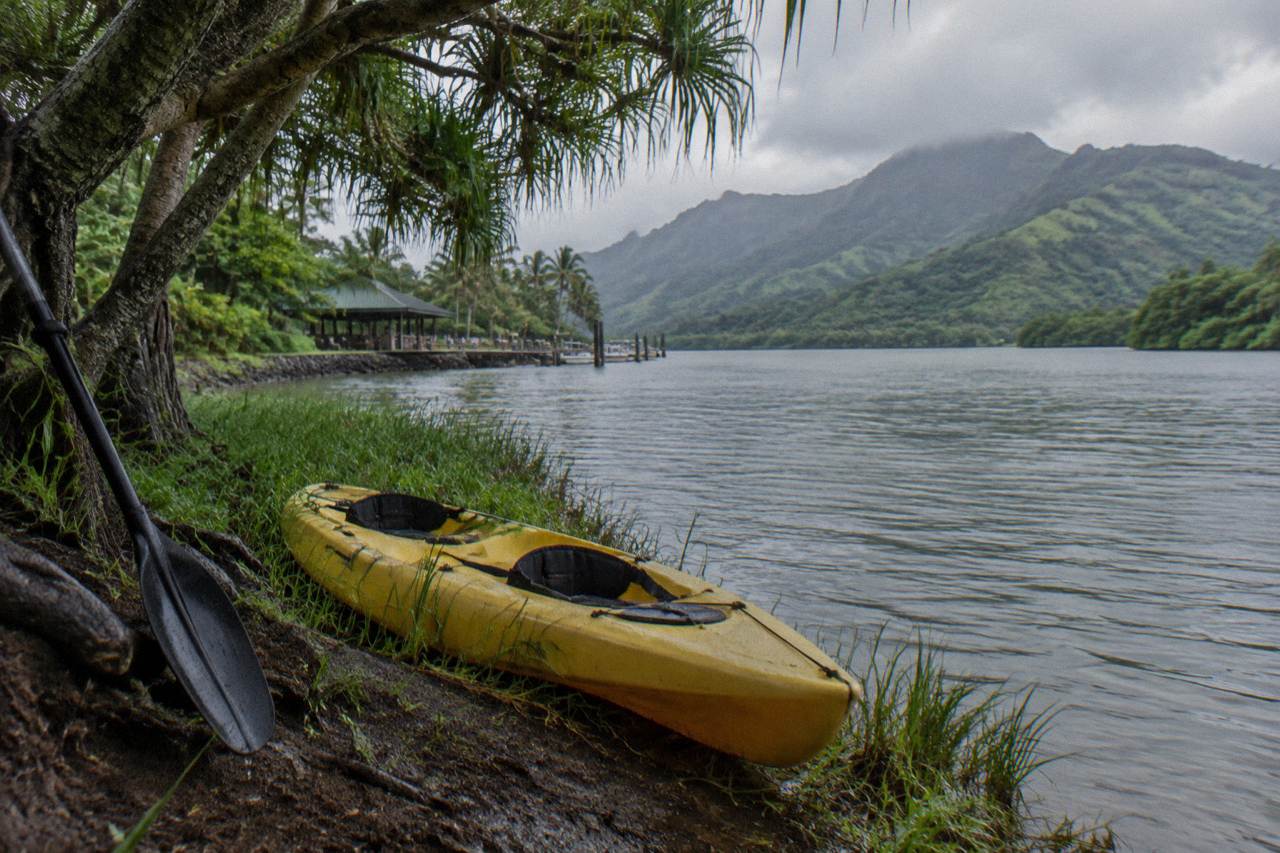 A tandem kayak resting on the bank of a wide jungle river with tall green mountain ridges behind it