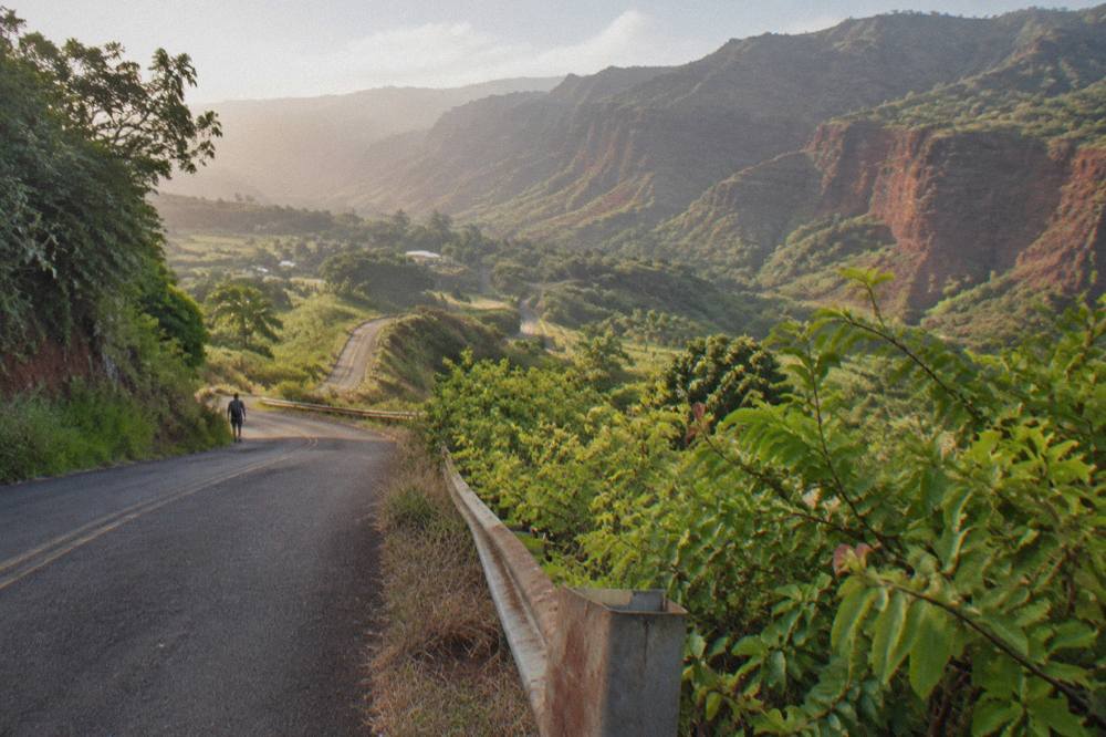 Winding mountain road climbing through green hills toward red canyon walls