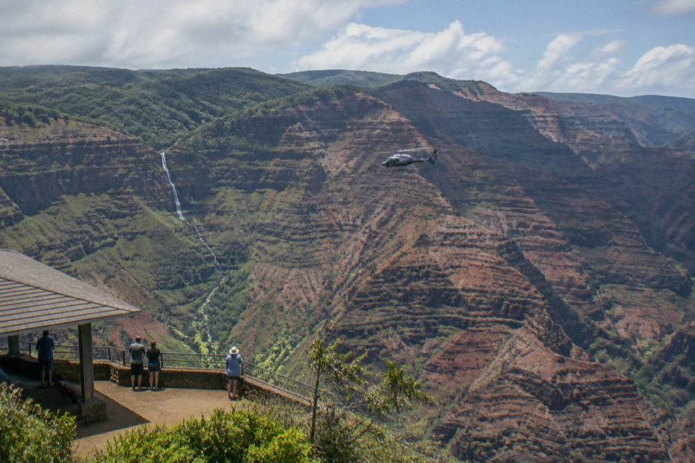Helicopter flying along red canyon cliffs with waterfall in the distance
